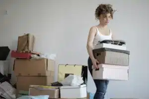 Woman carrying boxes and surrounded by more boxes